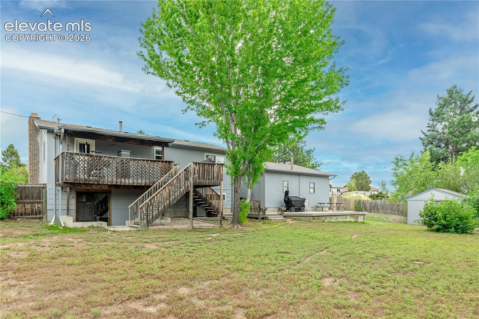 Spacious backyard featuring a multi-level wood deck, exterior staircase, masonry chimney, and detached storage structure