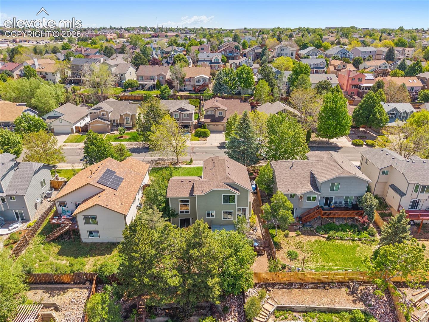 Residential property featuring a rear deck with direct yard access, mature trees, and a terraced landscape