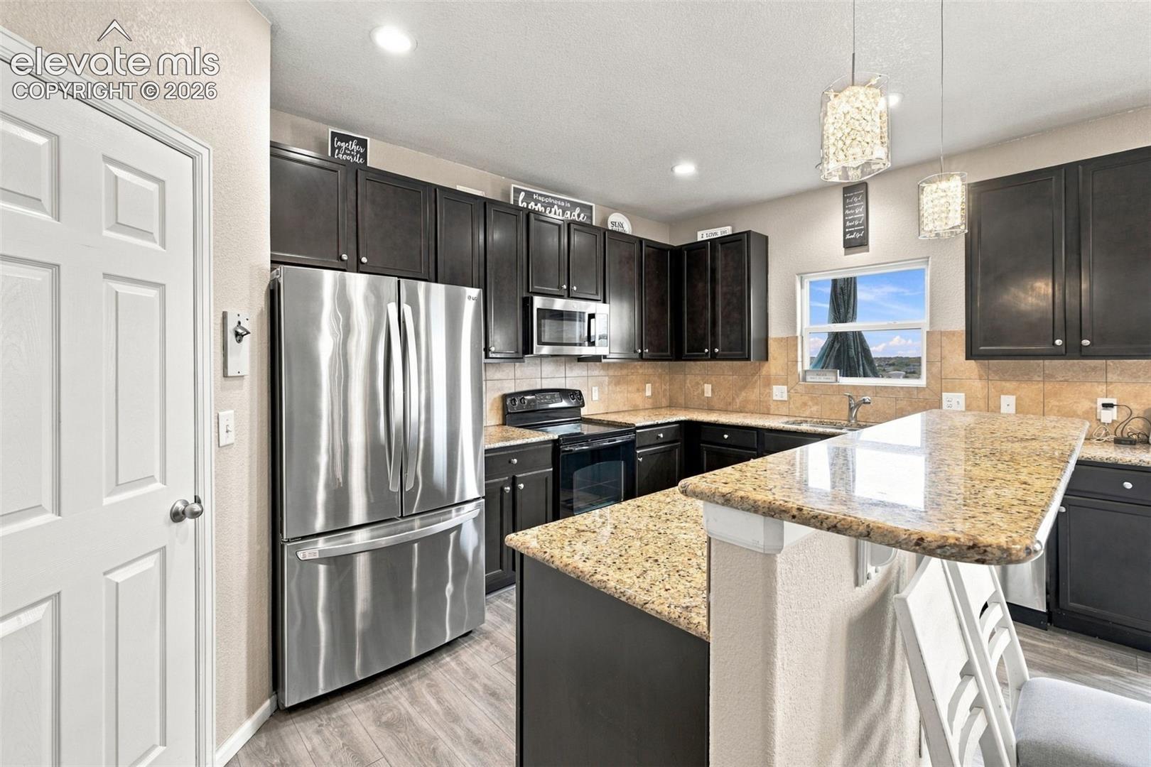 Kitchen featuring dark-finish cabinetry, stone-surface countertops, stainless steel appliances, a breakfast bar, and recessed lighting