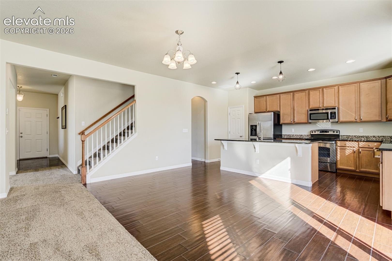 Open-concept floor plan featuring wood-finish flooring, a kitchen island with stone countertops, stainless steel appliances, and natural wood cabinetry