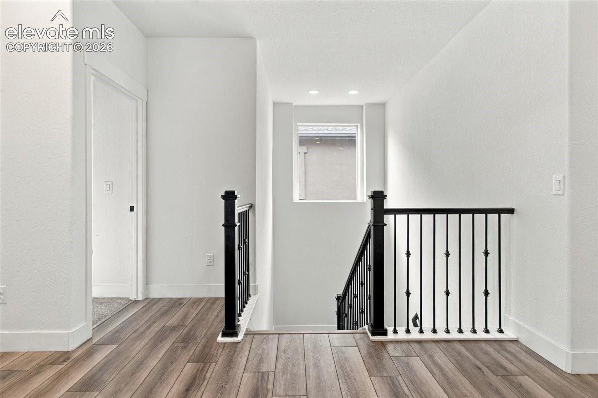 Wood-finish flooring, matte black metal balusters, square newel posts, recessed lighting, and a square window