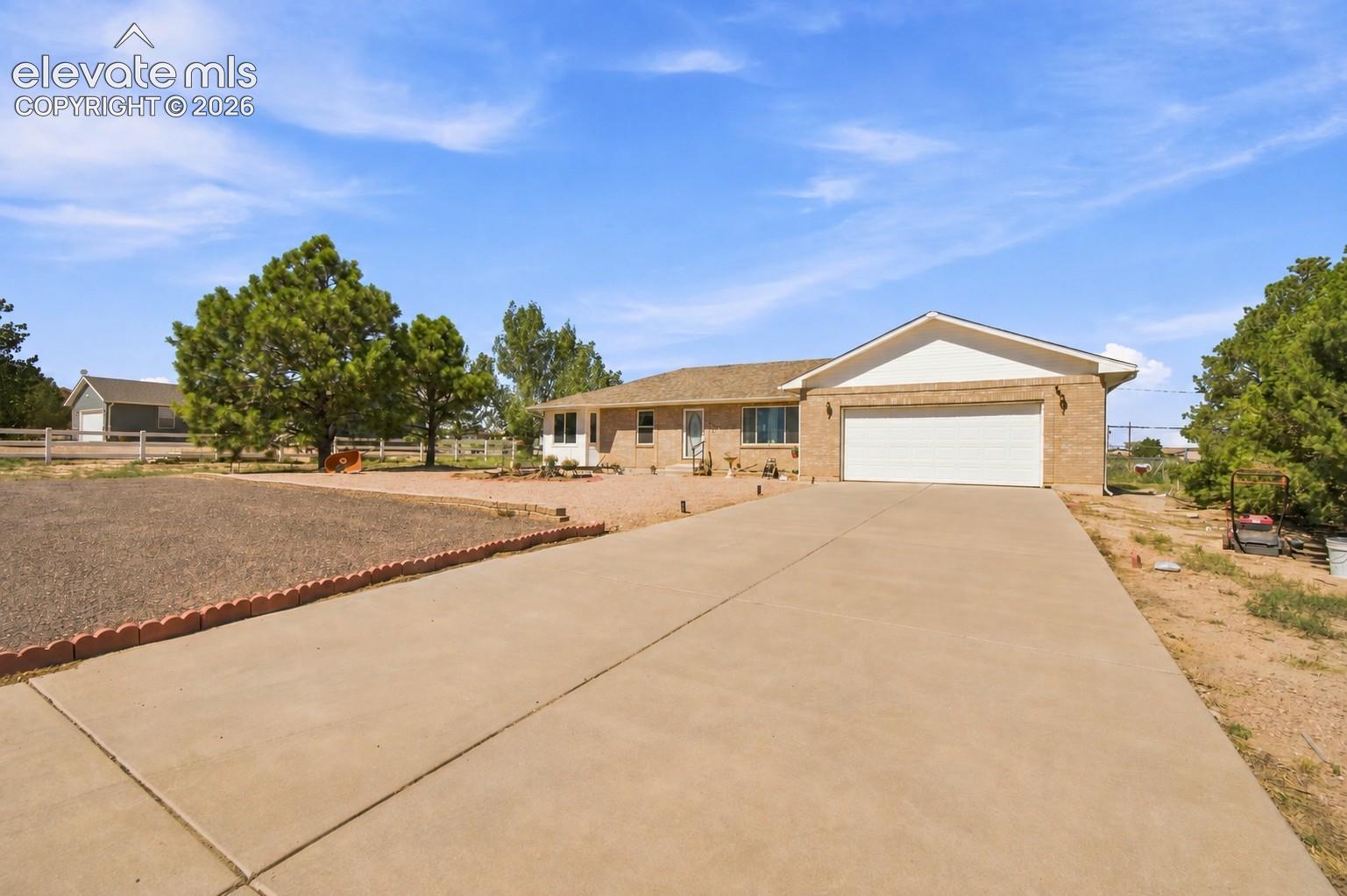 Brick-clad exterior with an attached two-car garage, concrete driveway, and mature landscaping