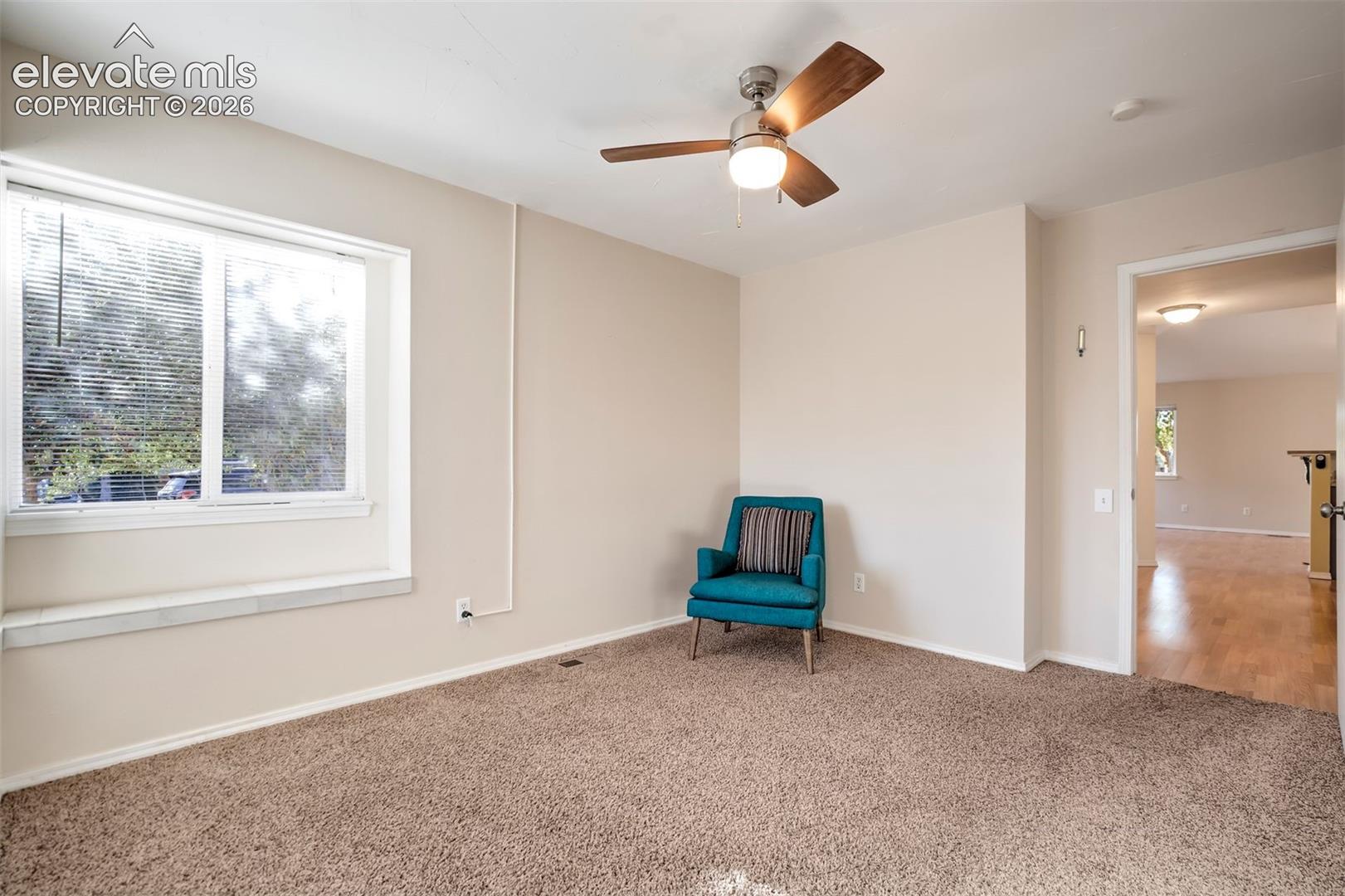 Neutral-toned room featuring a wide window seat, carpeted flooring, and a ceiling fan with integrated lighting