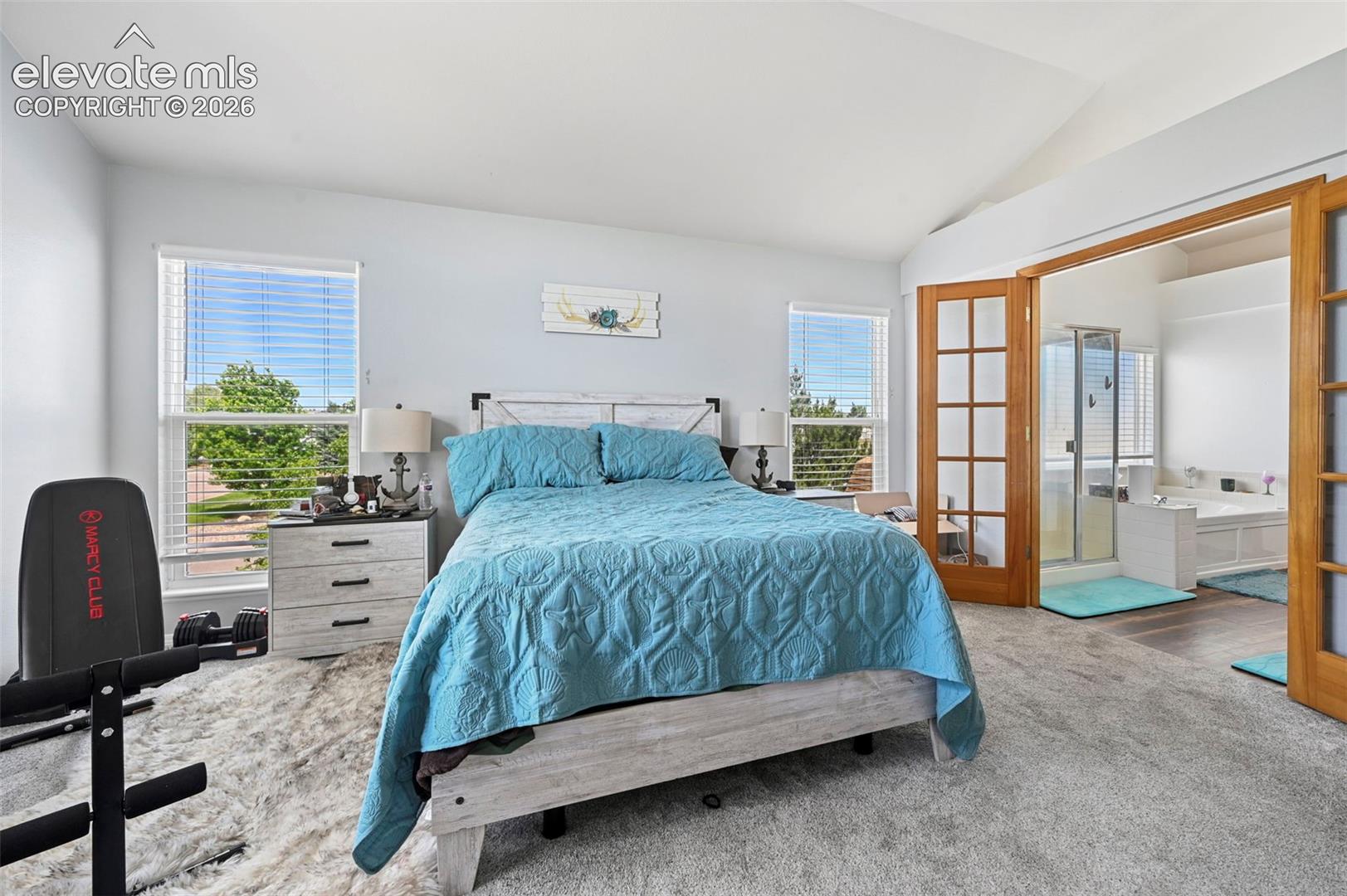 Spacious bedroom featuring vaulted ceilings, two large windows with horizontal blinds, and carpet flooring