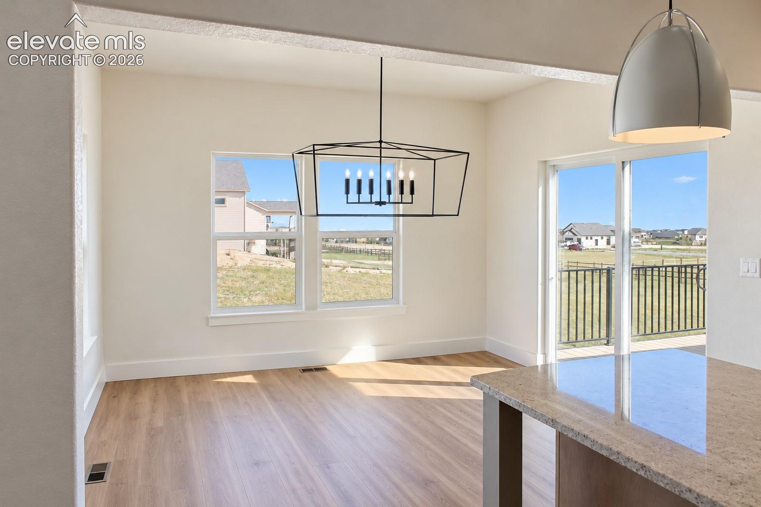 Open floor plan with wood-finish flooring, a contemporary geometric chandelier, and a sliding glass door leading to an outdoor area with a metal railing