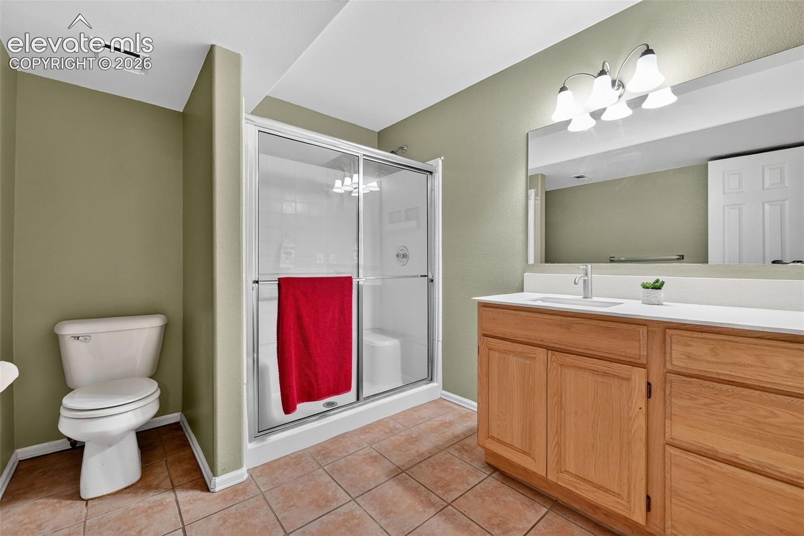 Bathroom featuring a wood-finish vanity with a rectangular sink, oversized wall-mounted mirror, walk-in shower with a glass enclosure, and ceramic tile flooring