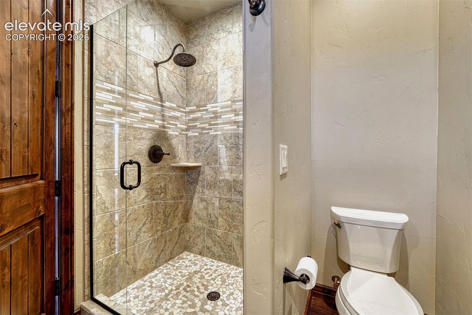 Glass-enclosed shower with stone tile surround, mosaic accent tile, and a pebble stone floor