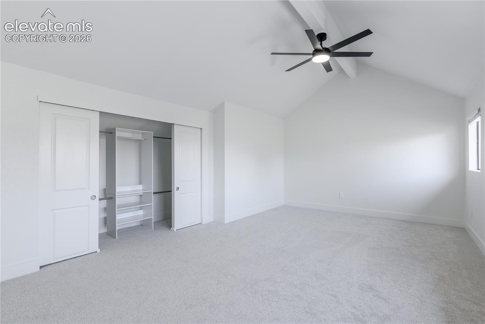 Vaulted ceilings with exposed beams, ceiling-mounted light fixture with fan, wall-to-wall carpeting, and built-in closet organization system