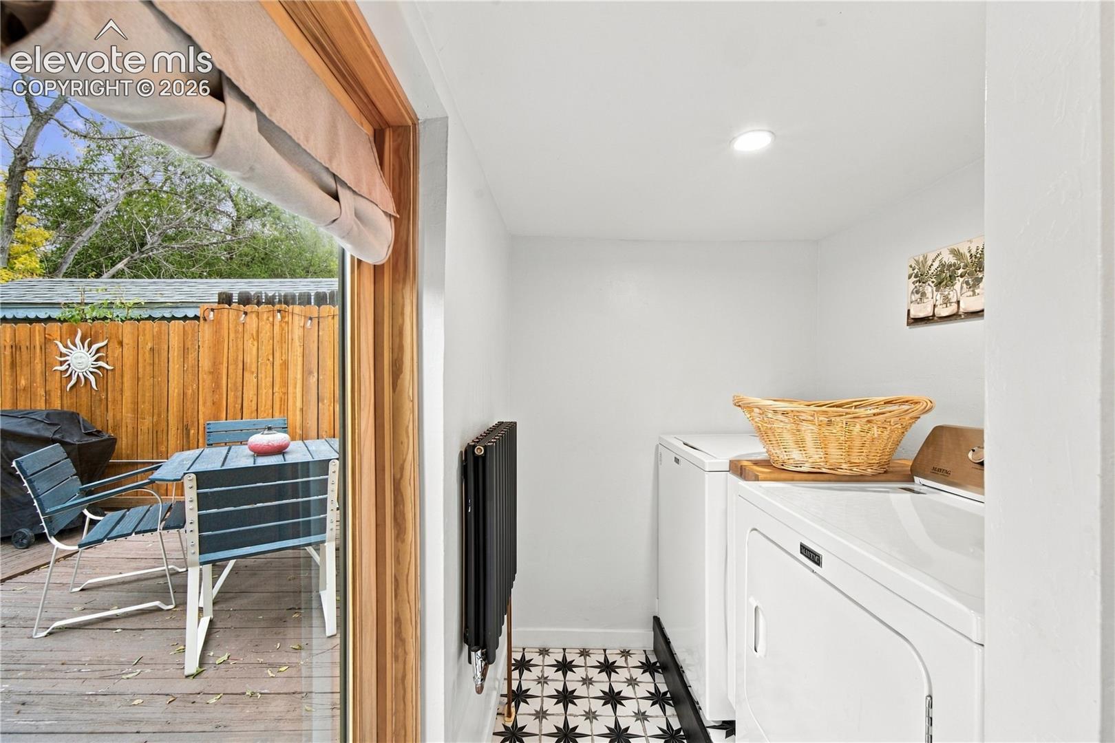 Utility area featuring patterned tile flooring, wall-mounted black radiator, and direct access to an outdoor wooden deck through a sliding glass door