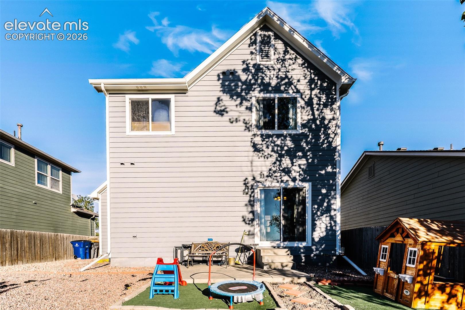 Exterior featuring light gray siding, white trim, multiple windows, a sliding glass door, and an upper-level gable
