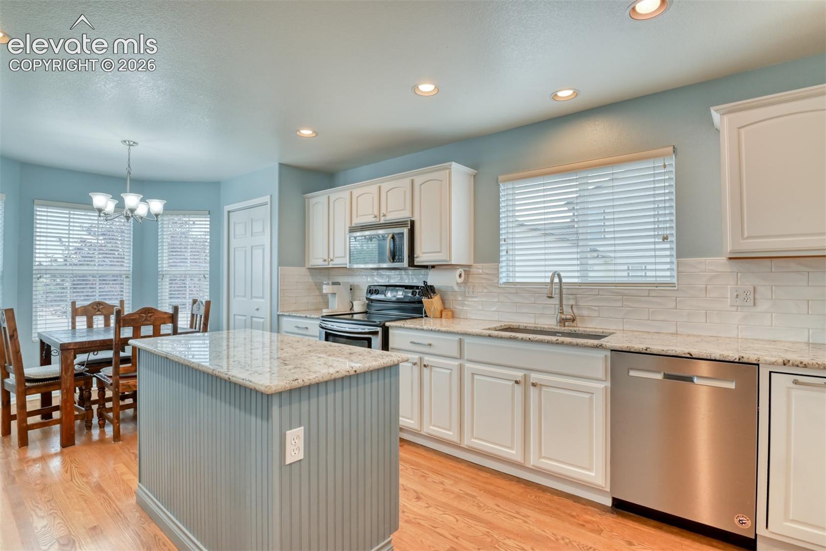 Hardwood flooring, recessed lighting, white cabinetry, integrated stainless steel appliances, and a beadboard kitchen island with a light-toned countertop