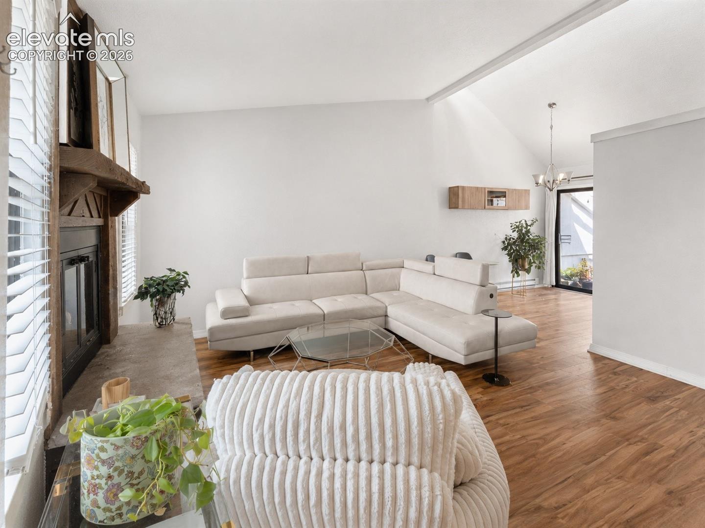 Living area featuring wood-finish flooring, a fireplace with a stone hearth and wood mantle, vaulted ceilings, and a light-colored wall finish