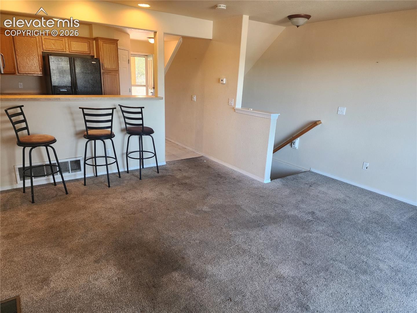 Open-concept living space featuring a breakfast bar, kitchen with wood cabinetry, and a staircase with a wood handrail