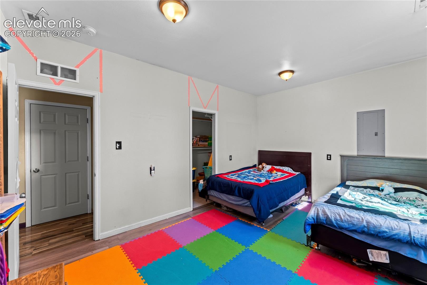 Room featuring wood-finish flooring, two flush-mount ceiling light fixtures, and two interior doors with six-panel detailing