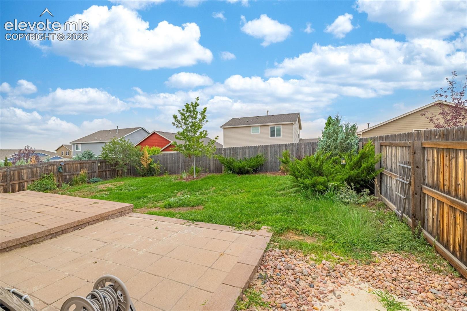 Expansive backyard featuring a stone paver patio, a wood privacy fence, and diverse plantings