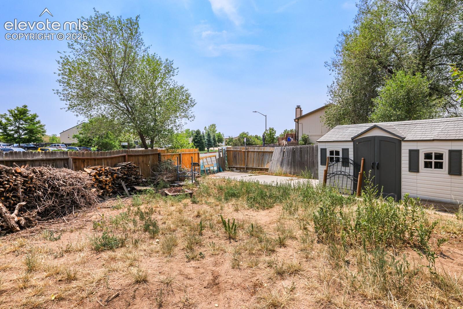 Spacious backyard area featuring a wood fence, a large storage shed with faux windows and shutters, and mature trees