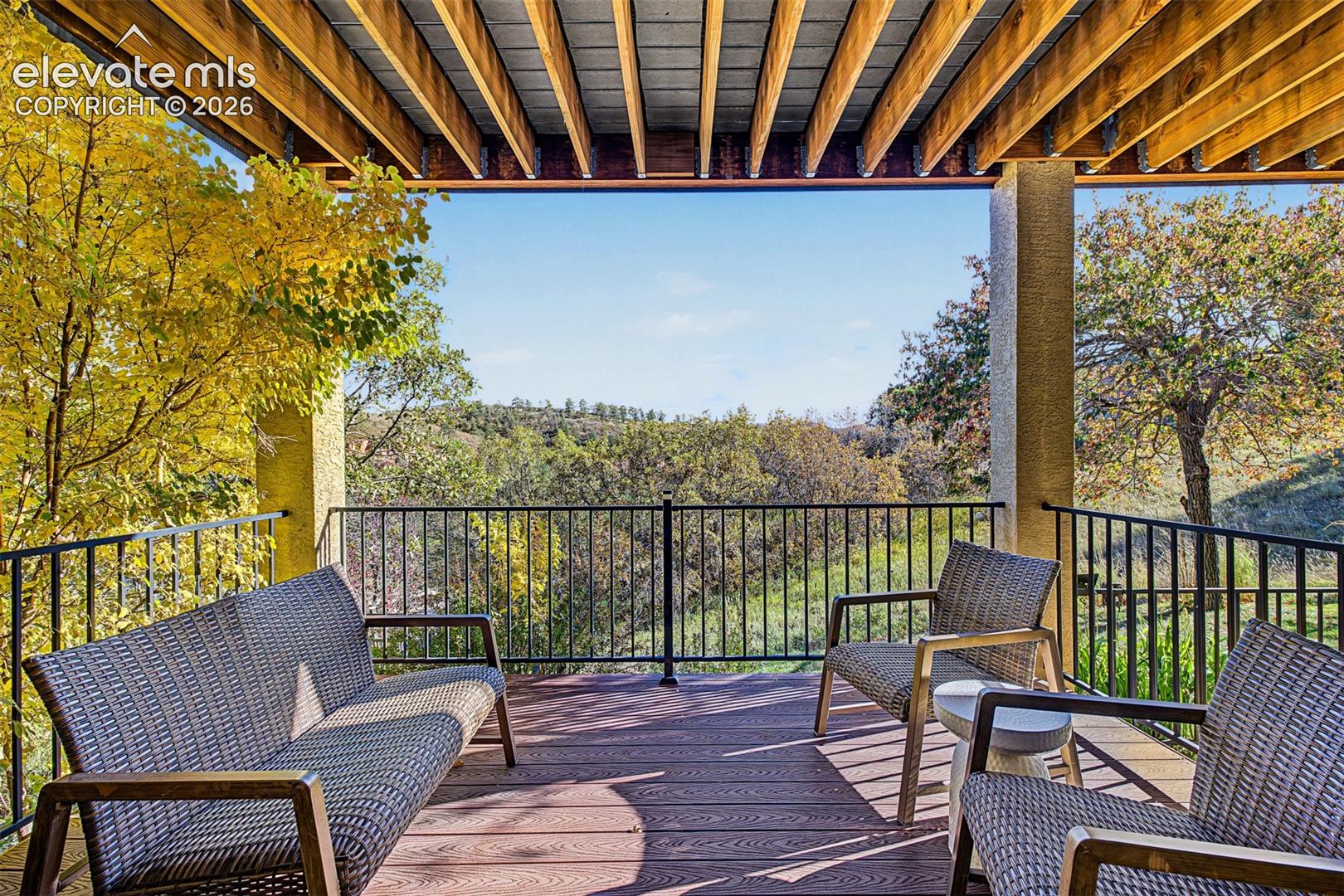 Spacious covered patio just outside the walkout basement, beneath the main-level balcony, offering a peaceful outdoor retreat with views of the surrounding wooded foothills and mature trees.