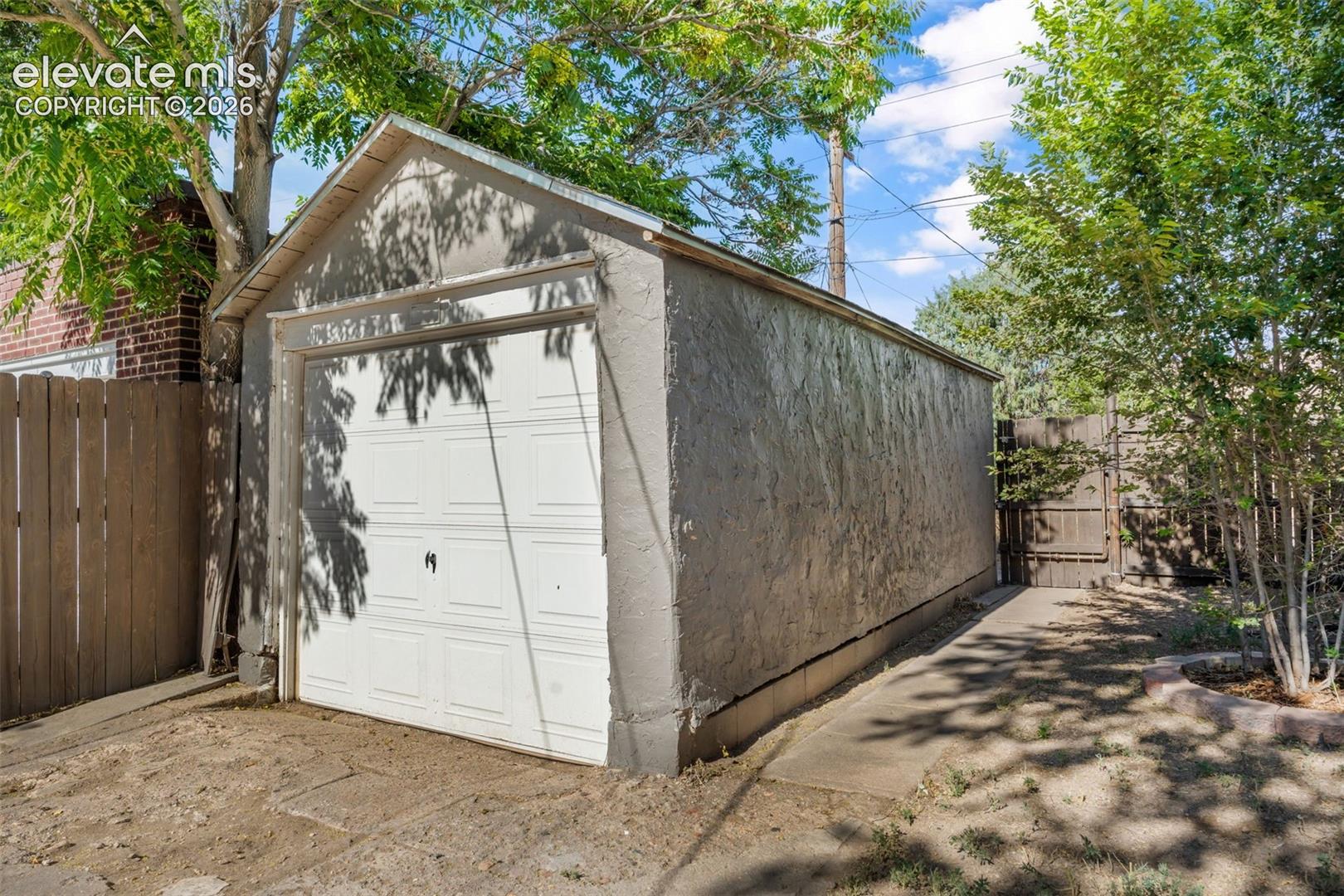 Detached single-car garage featuring a white panel door and stucco exterior