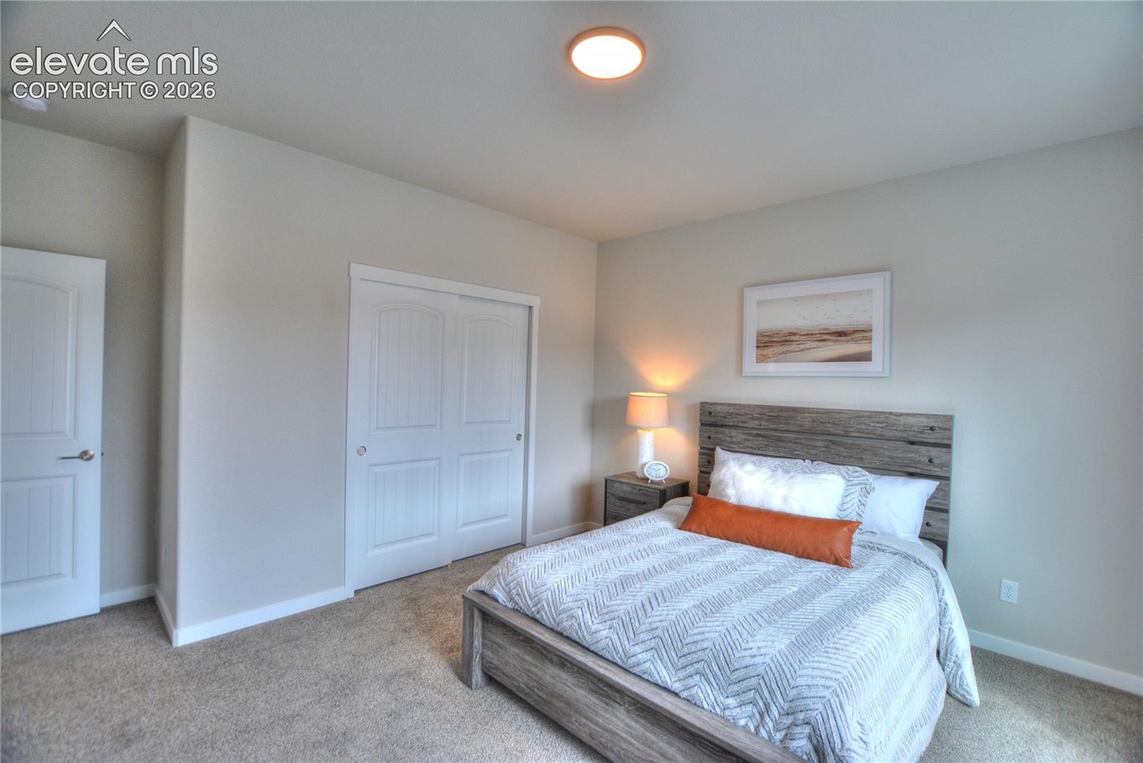 Spacious bedroom featuring a wood-finish platform bed, dual nightstands with integrated lighting, carpeted flooring, and abundant natural light from recessed ceiling fixtures