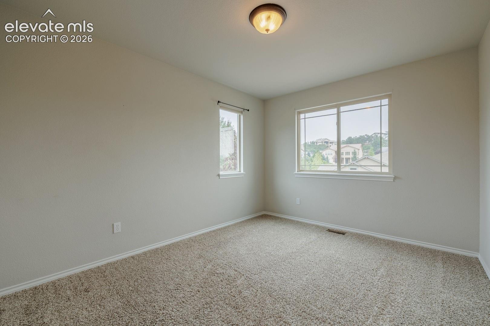Bright bedroom offering abundant natural light through dual windows, neutral wall finishes, and soft neutral carpeting