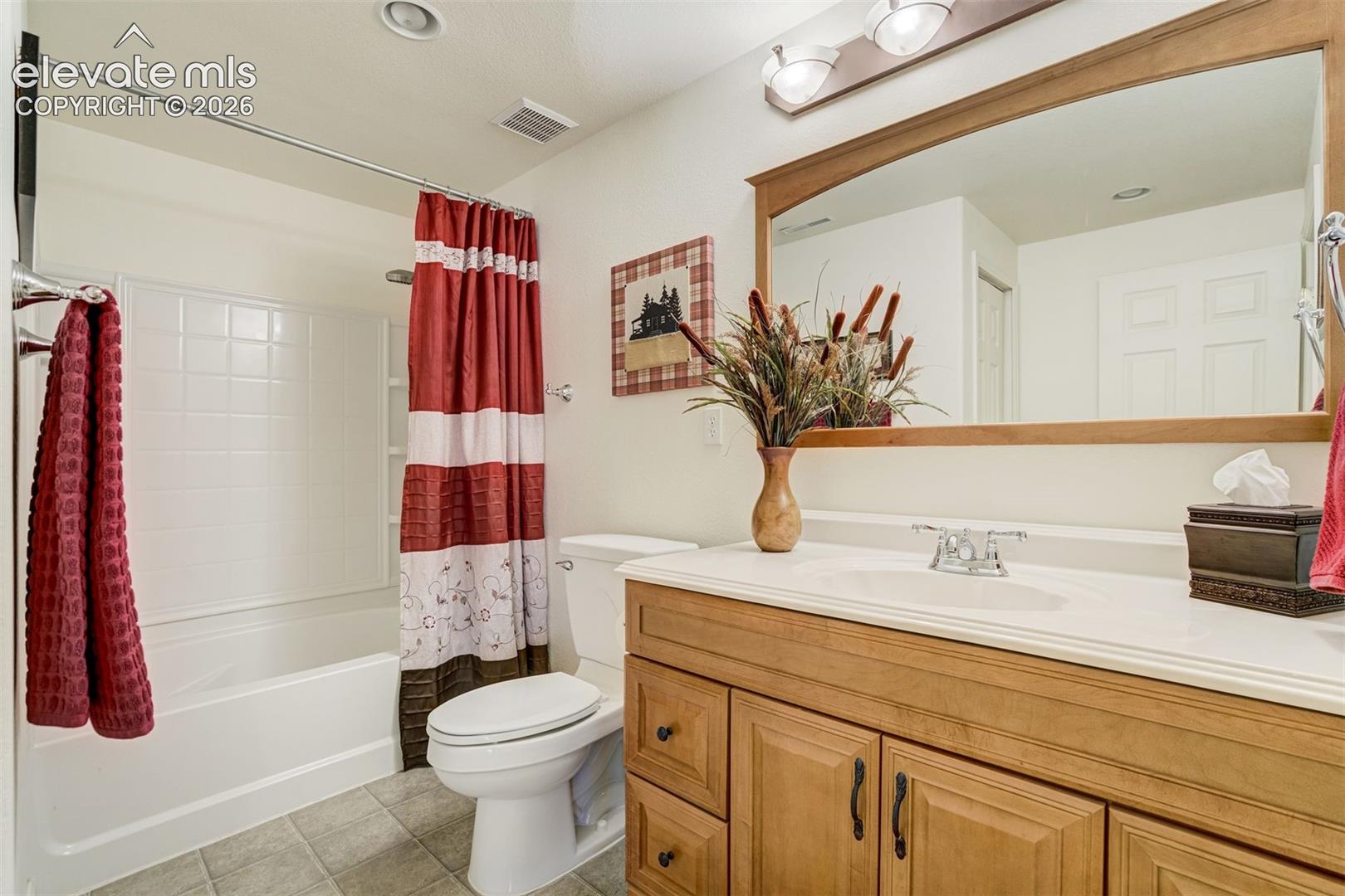 Bathroom featuring a wood-finish vanity with an integrated basin, a large wood-framed mirror, chrome faucet hardware, and a white tiled shower surround