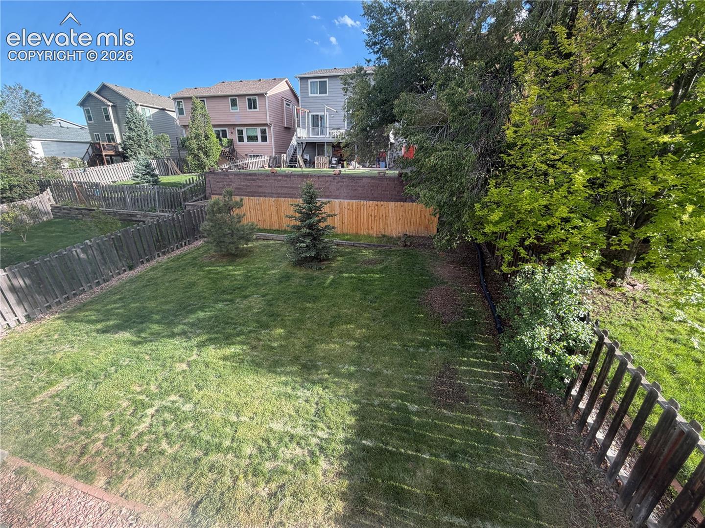 Backyard featuring a large grass lawn, mature trees, and wood fencing
