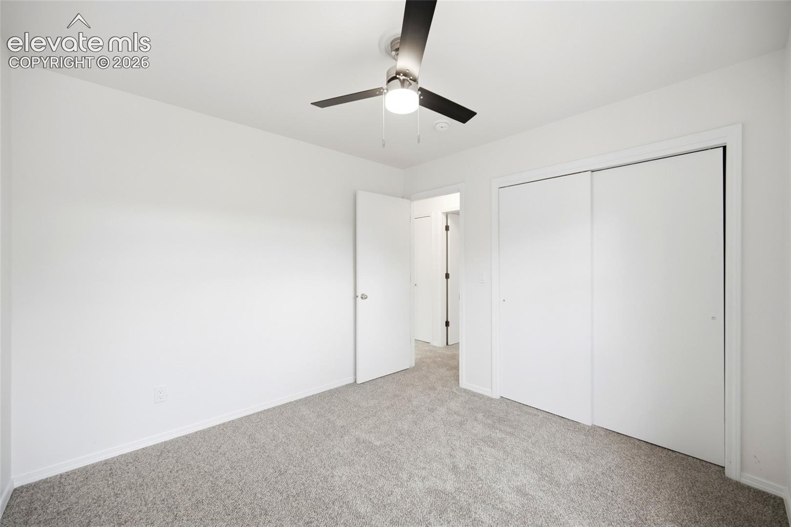 Neutral-toned wall-to-wall carpeting, modern three-blade ceiling fan with integrated lighting, and dual-panel sliding closet doors