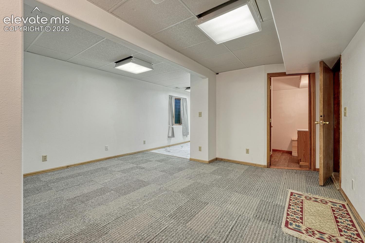Spacious room featuring patterned carpeting, white walls, wood trim, and recessed lighting