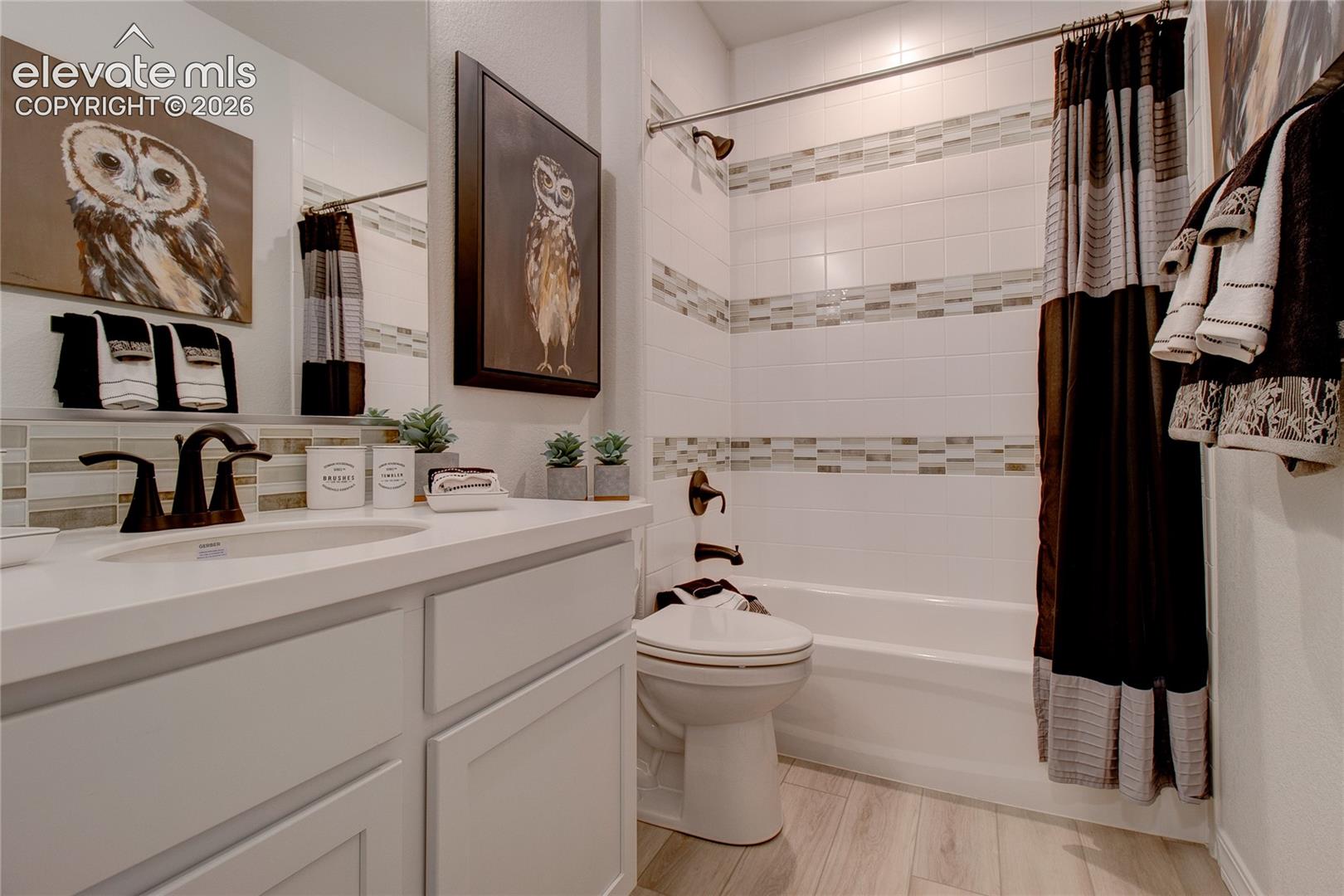 White vanity cabinet featuring a solid surface countertop with an integrated basin, bronze-finish faucet, tub and shower fixtures, and decorative horizontal tile backsplash