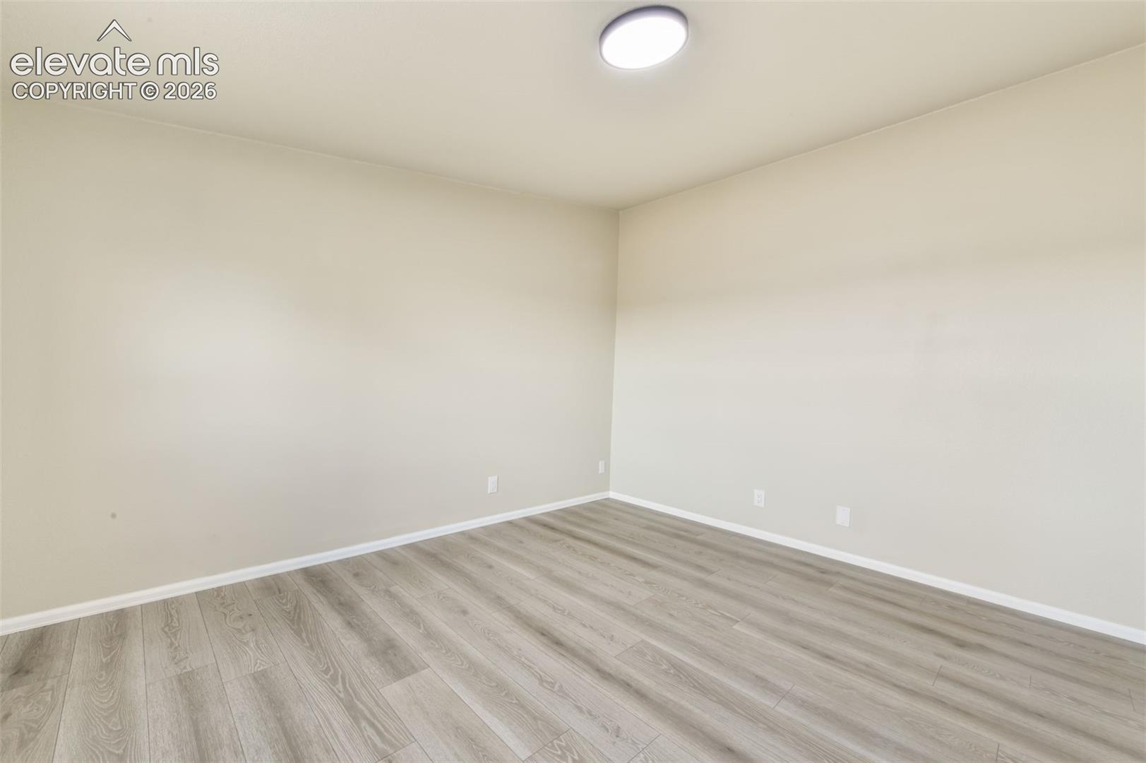Light-toned walls with wood-finish flooring, featuring a flush-mount ceiling light