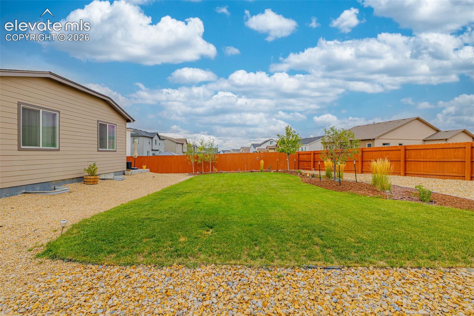 Expansive backyard featuring a manicured lawn, gravel perimeter, mature trees, and a wooden privacy fence