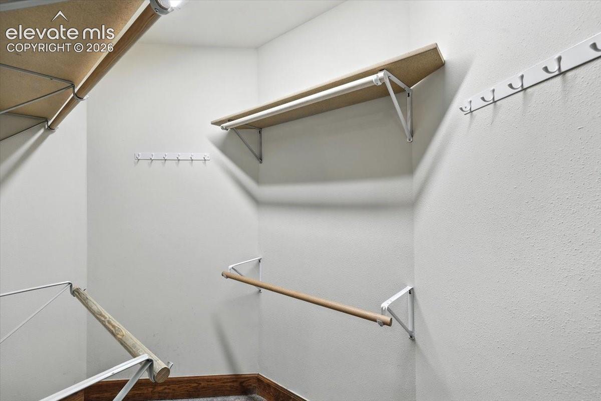Walk-in closet featuring tiered wood-finish shelving, wall-mounted metal clothing rods, and installed hardware for additional organization