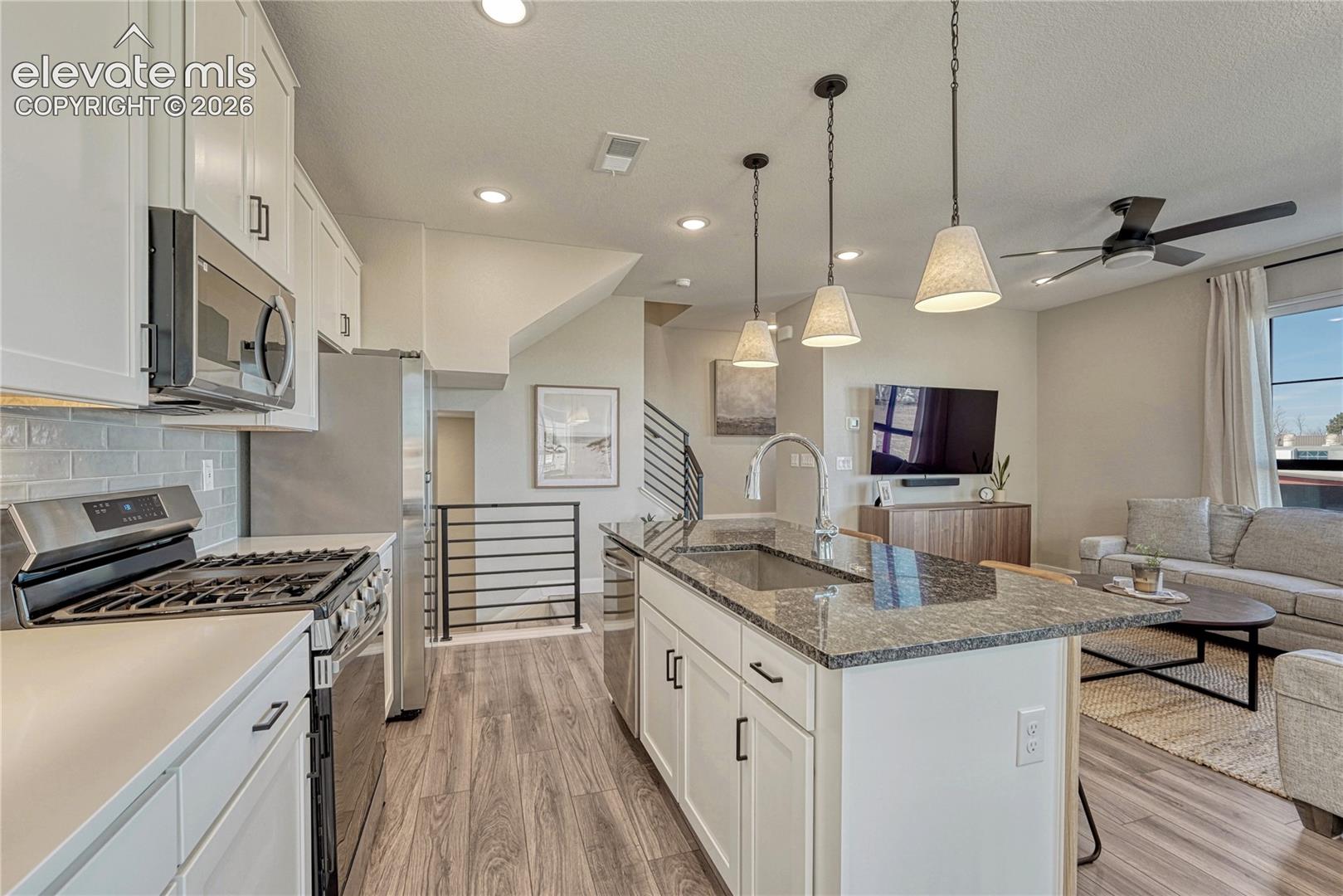 Kitchen featuring white cabinetry, stone-surface island with integrated sink, stainless steel appliances, wood-finish flooring, and industrial-style pendant lighting