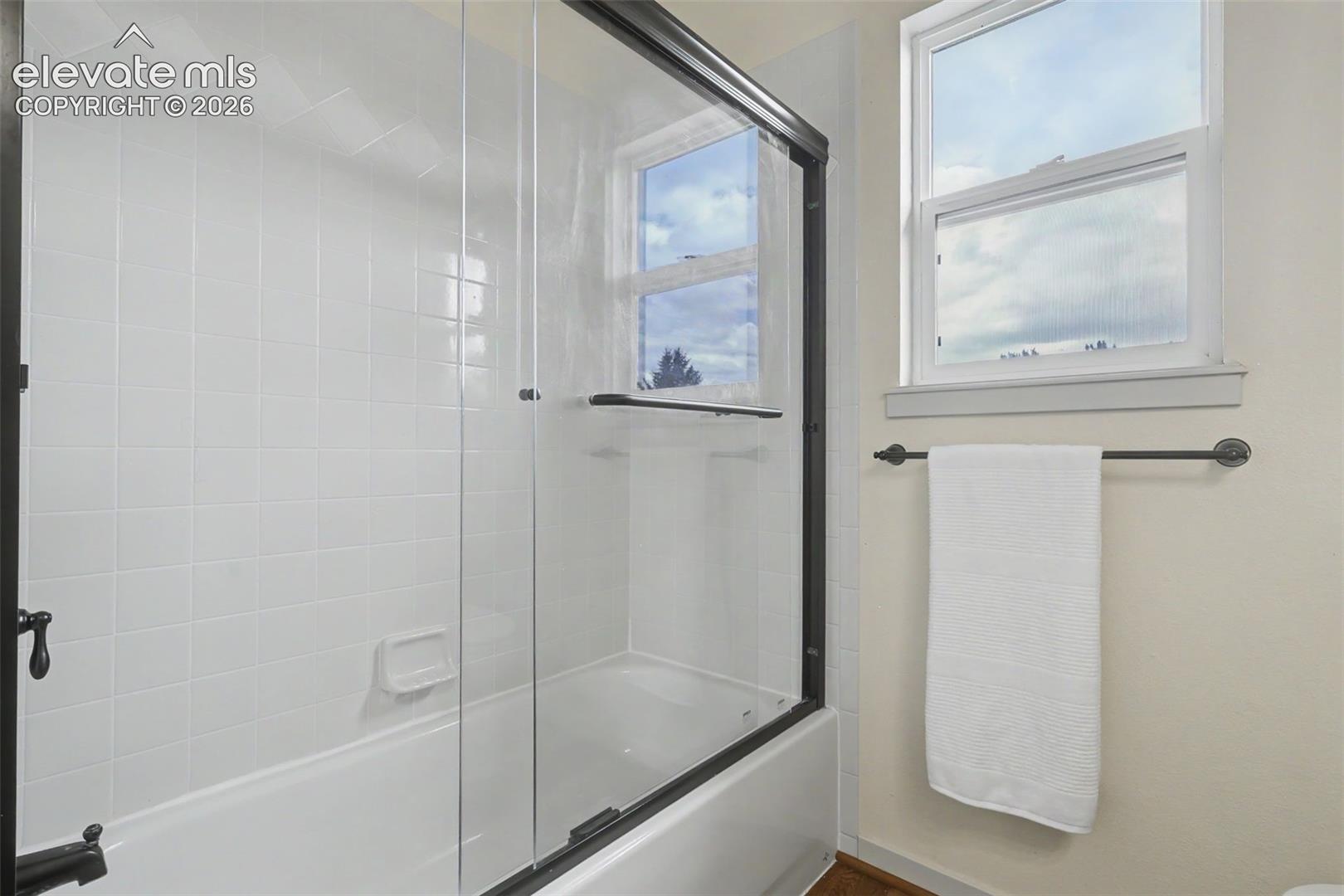 Bathtub-shower combination featuring a clear glass enclosure with dark bronze framing