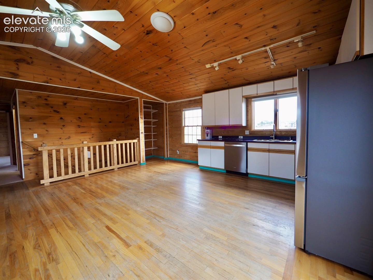 Wood-paneled vaulted ceiling and walls, white cabinetry with dark countertops, stainless steel appliances, wood-finish flooring, and built-in shelving
