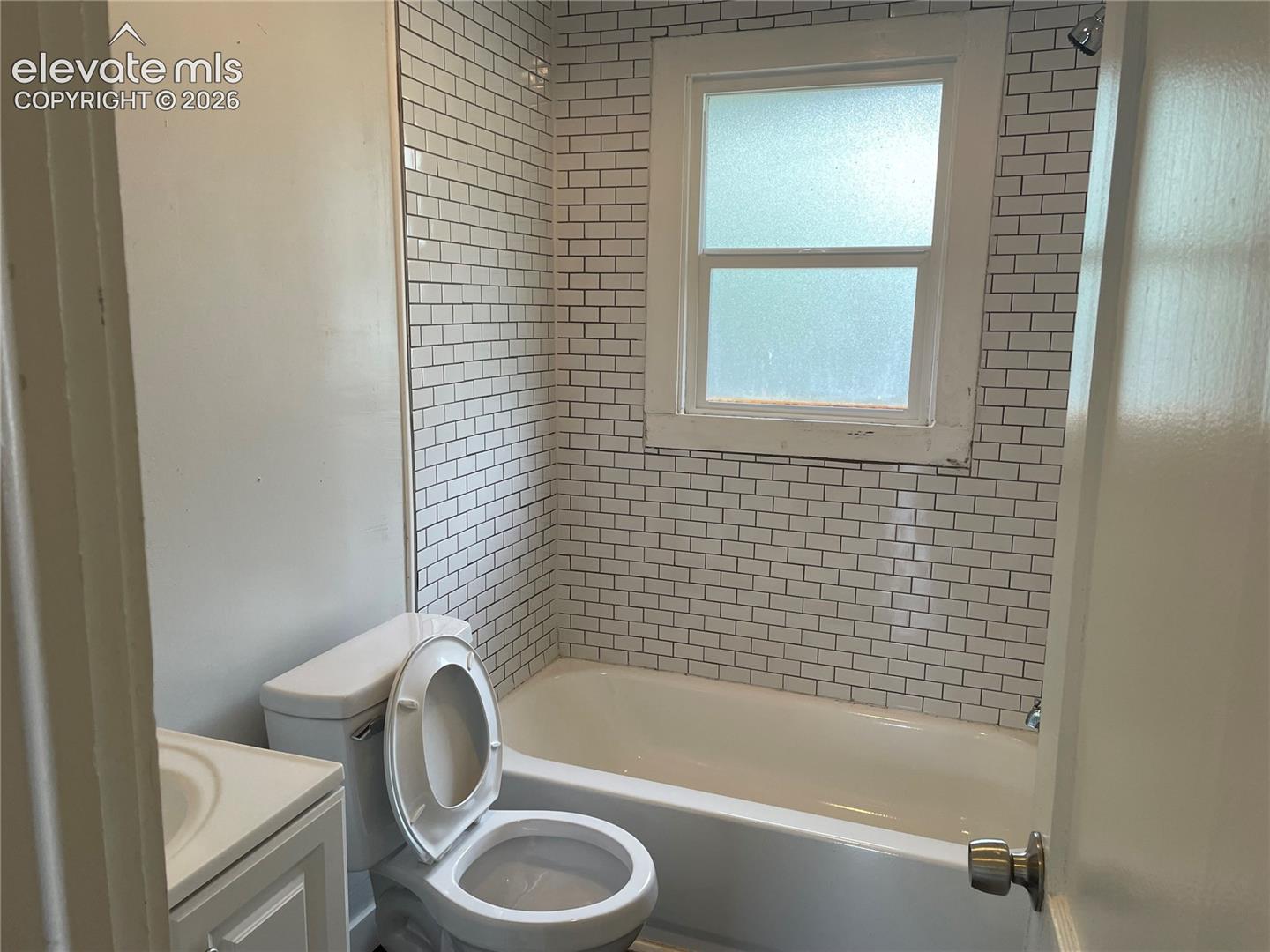 Bathroom featuring a white subway tile surround, white bathtub, and a window with opaque glass