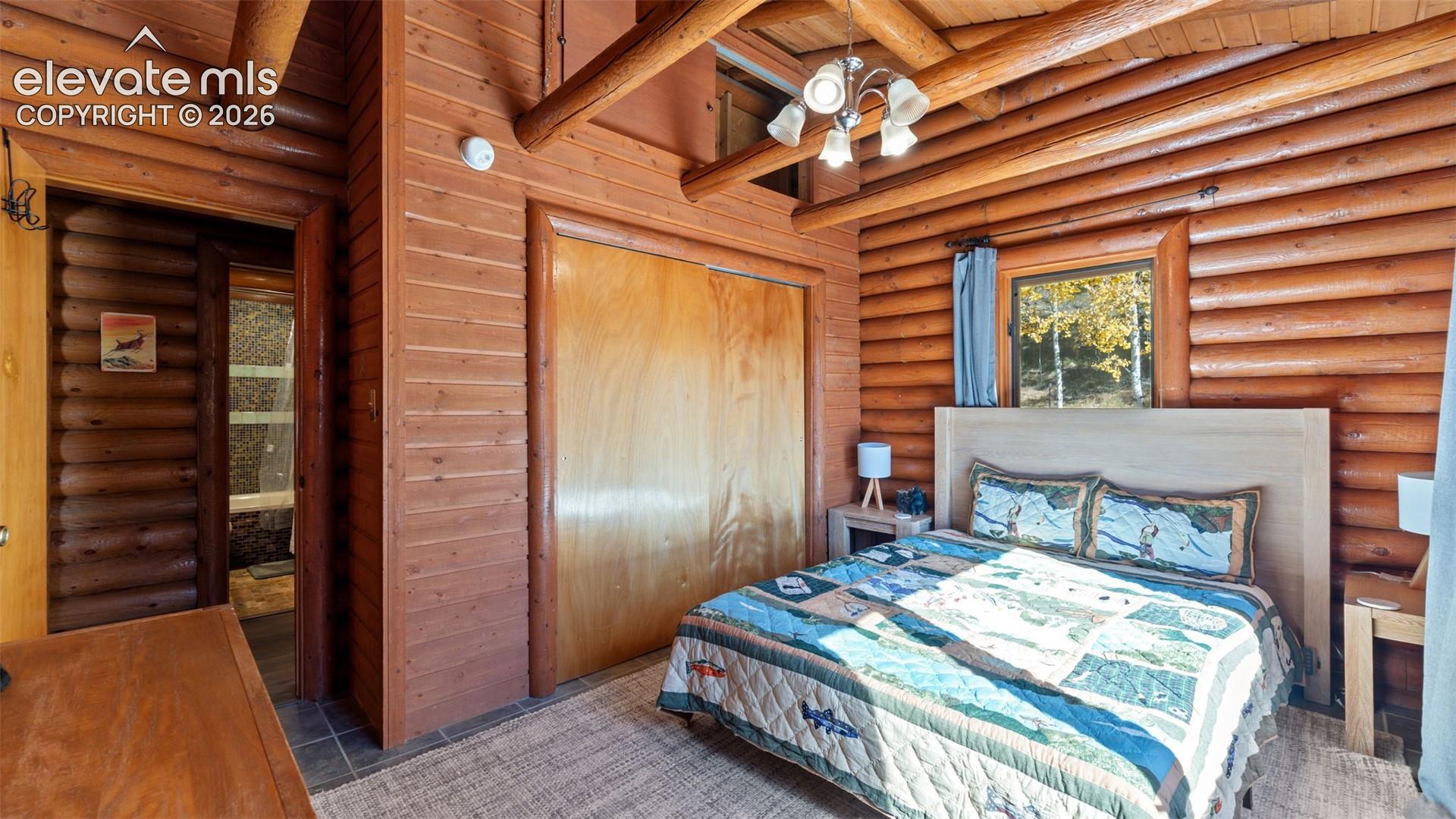 Exposed log walls, vaulted timber-beam ceiling, integrated sliding-door closet, and five-light multi-arm ceiling fixture