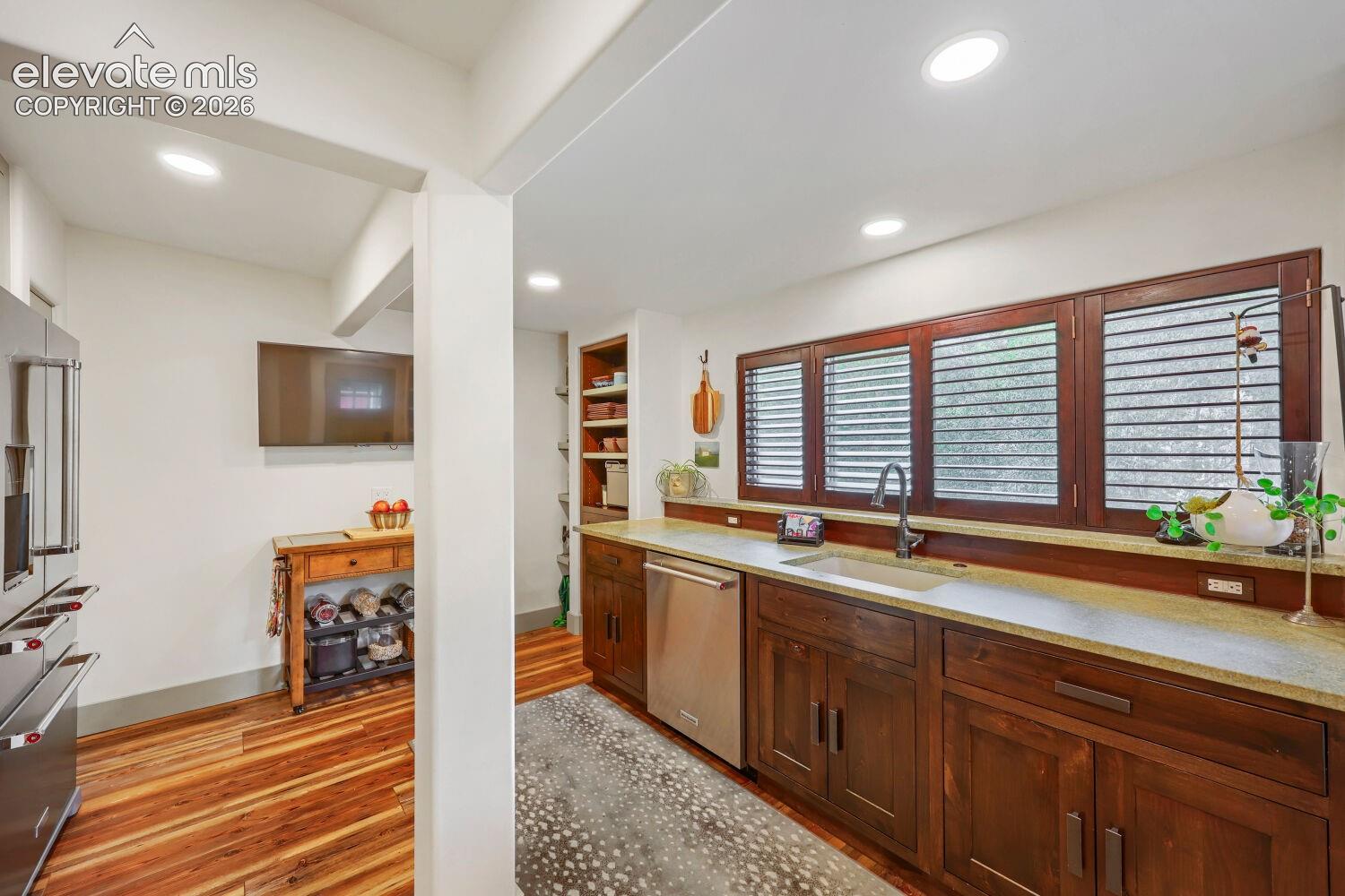Recessed lighting illuminates the kitchen, featuring stainless steel appliances and wood-finish flooring