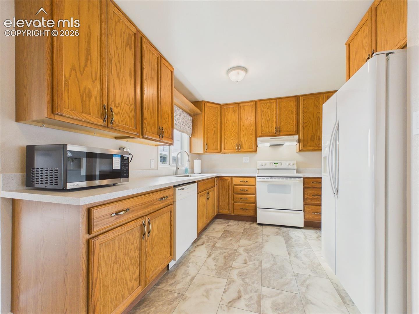 Closer view of the kitchen featuring oak cabinetry, ample countertop workspace, a built-in dishwasher, and a window overlooking the outdoors.