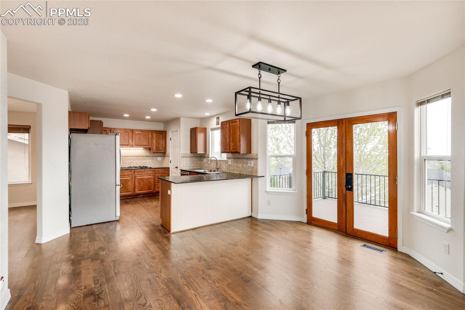 Spacious open-concept kitchen and breakfast area featuring wood-finish flooring, a kitchen island with beadboard paneling, rich wood cabinetry, stainless steel appliances, and double glass-paneled doors opening to an exterior balcony