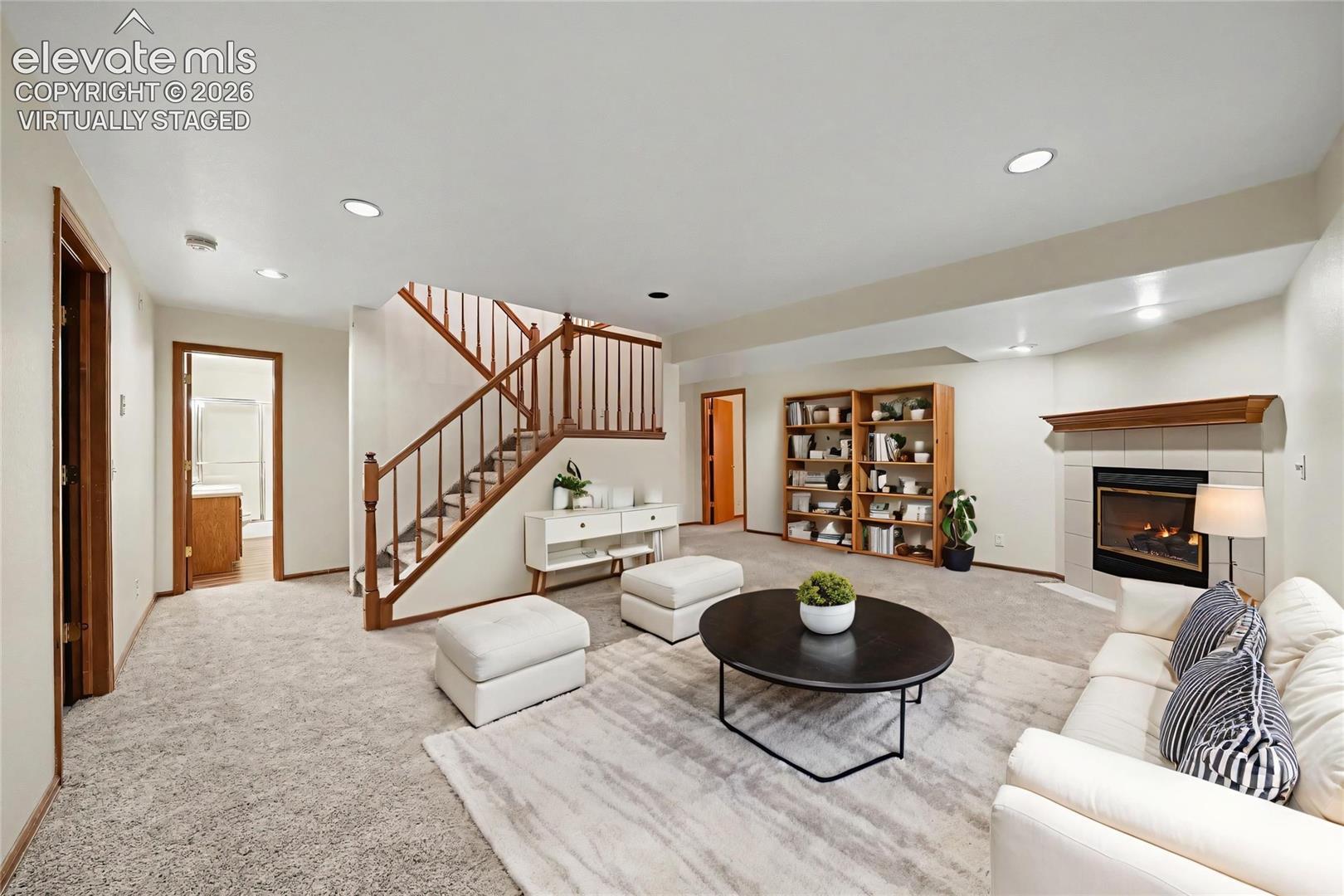 Virtually staged. Fireplace with tile surround and wood mantle, recessed lighting, built-in shelving, carpeted flooring, and a wood staircase with balusters