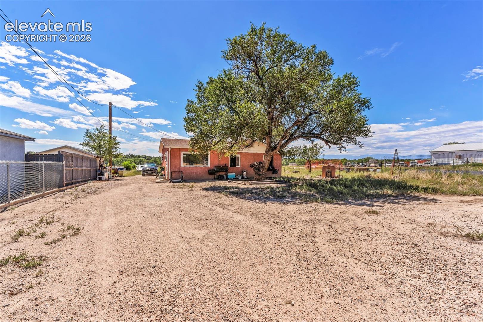 Expansive gravel lot with mature shade tree, chain link fencing, and a red stucco exterior