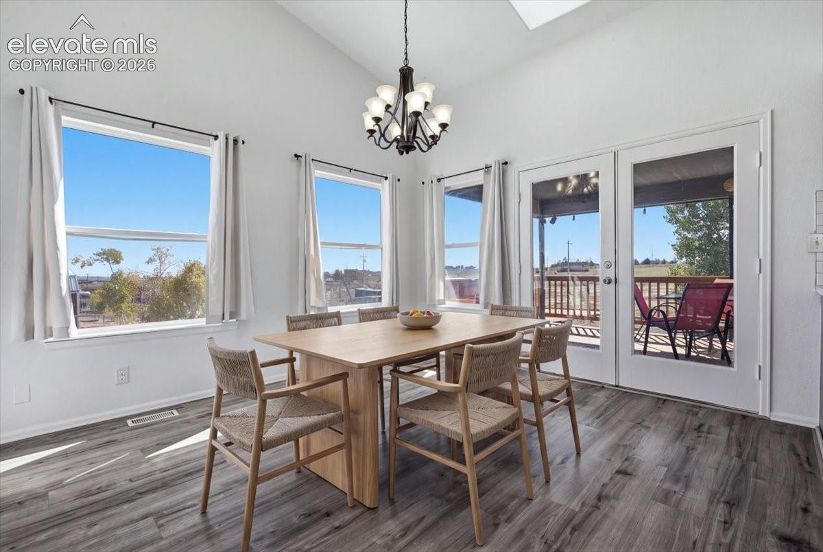 Vaulted ceiling featuring a skylight, wood-finish flooring, multi-light chandelier, and double glass doors leading to an exterior deck