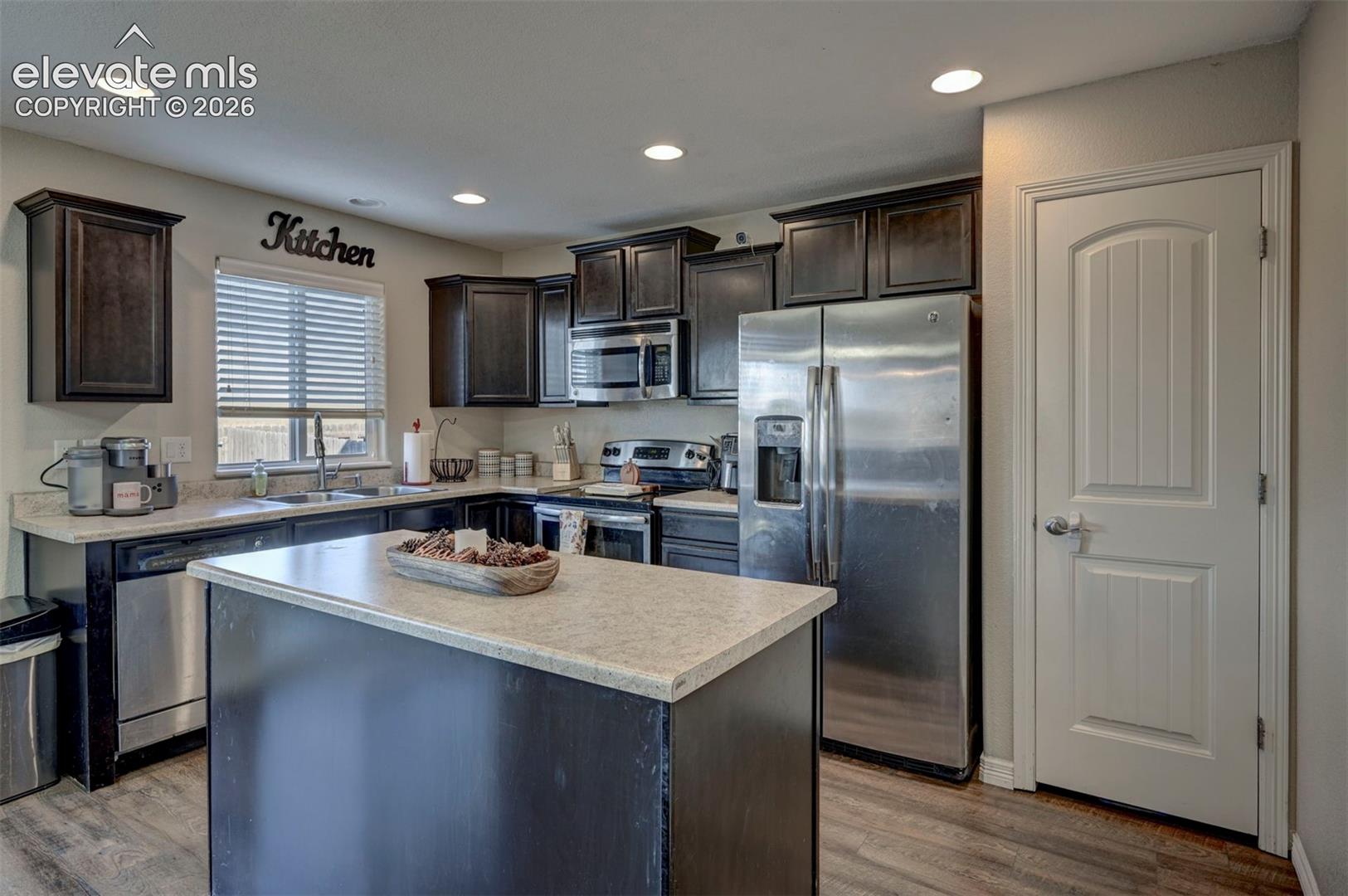 Spacious kitchen featuring an island with a light-toned countertop, dark wood-finish cabinetry, stainless steel appliances, and recessed lighting
