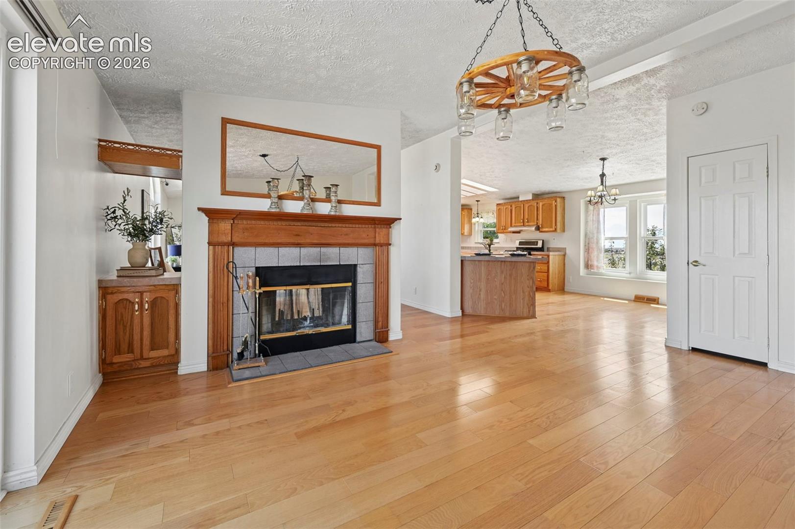 Hardwood flooring throughout, a fireplace with a wood mantel and tile surround, a built-in cabinet with wood-finish countertop, and a wagon wheel-style chandelier