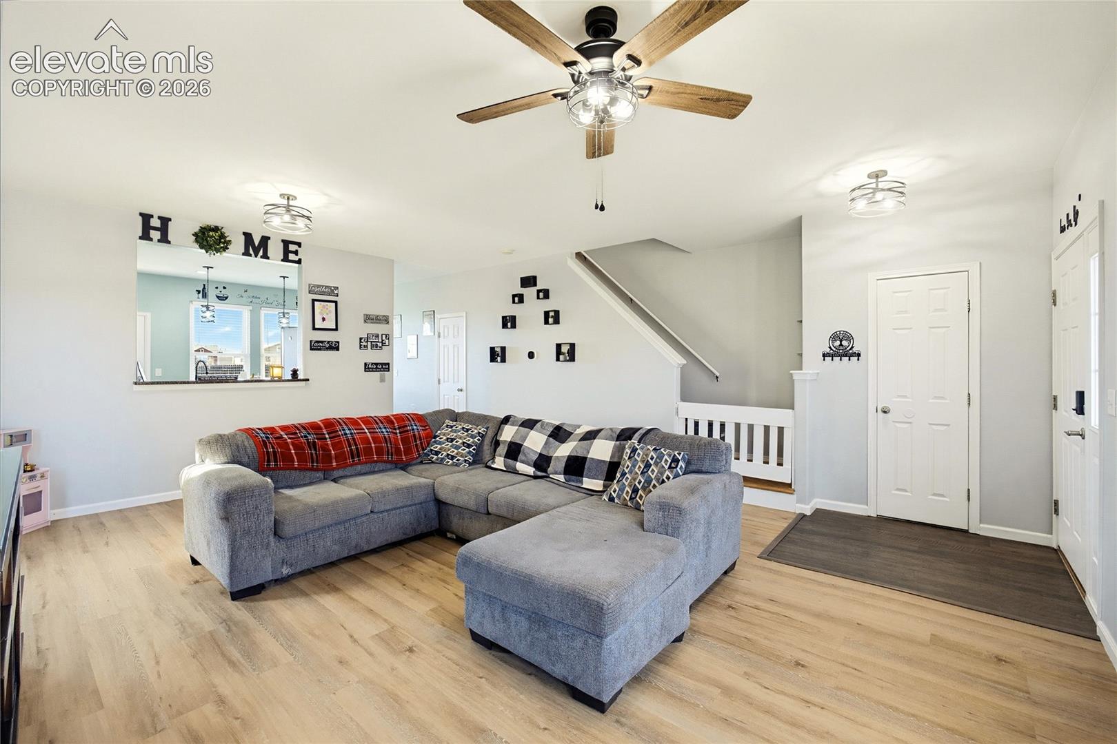 Wood-finish flooring throughout, ceiling fan with light kit, recessed wall opening, white paneled doors, and staircase with white railing