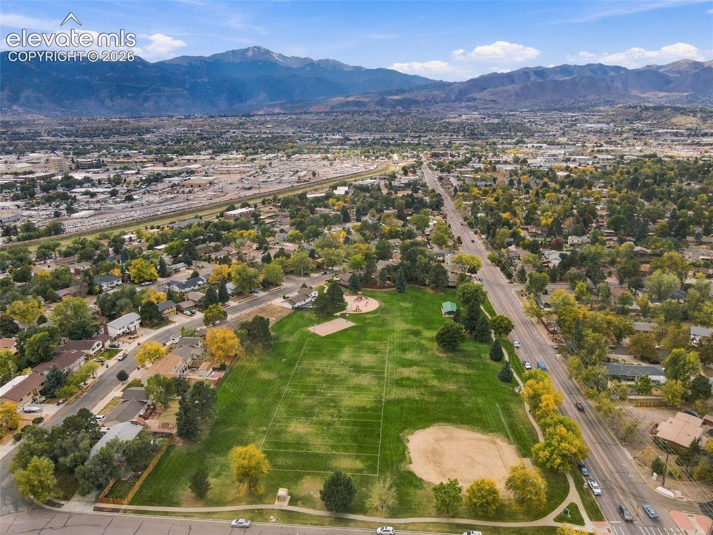 Aerial perspective showcasing an expansive park area featuring open green space, a baseball diamond, and mountain range backdrop