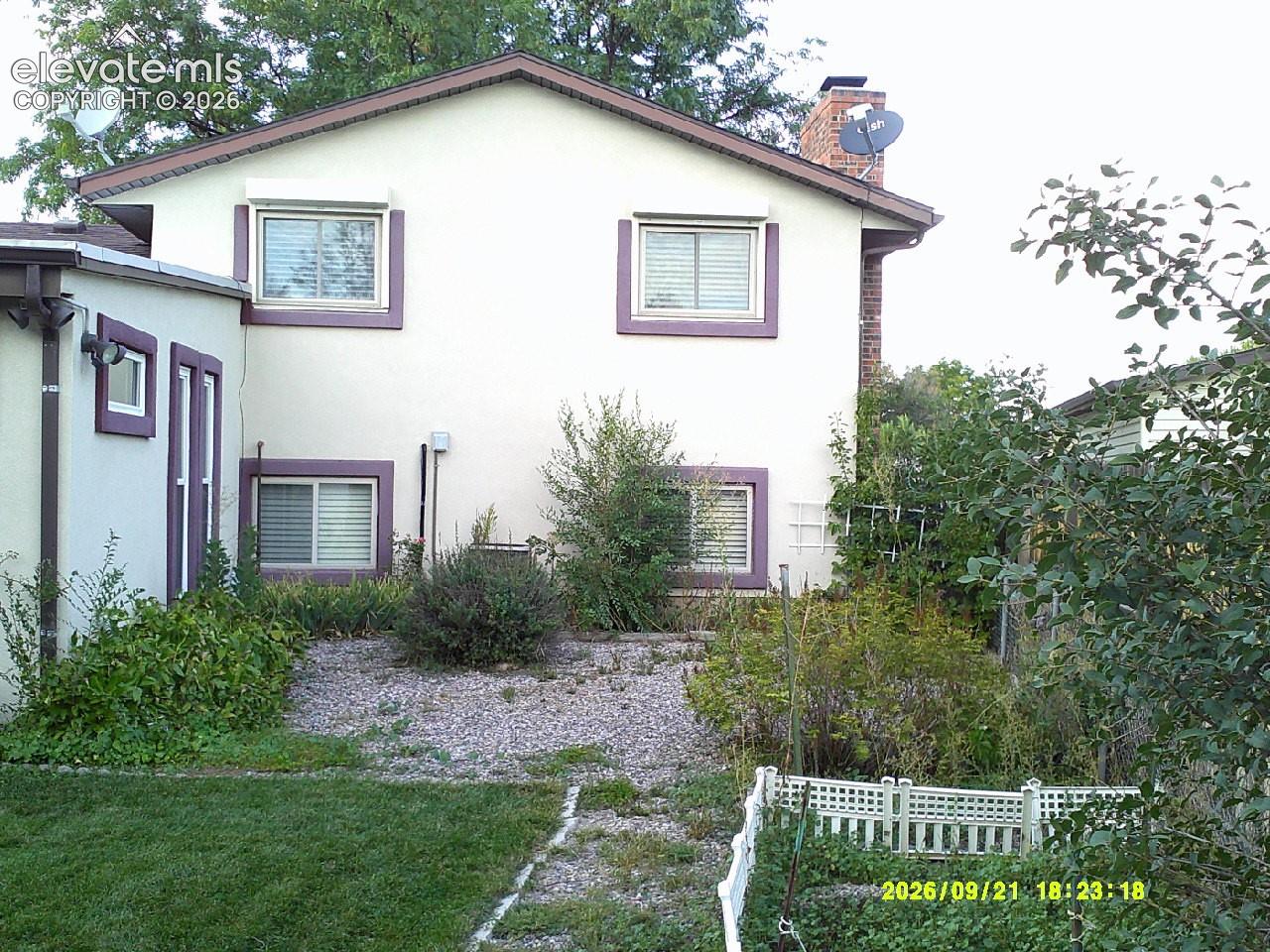 Stucco exterior with contrasting trim, multiple windows with blinds, pitched roof, and an exterior brick chimney