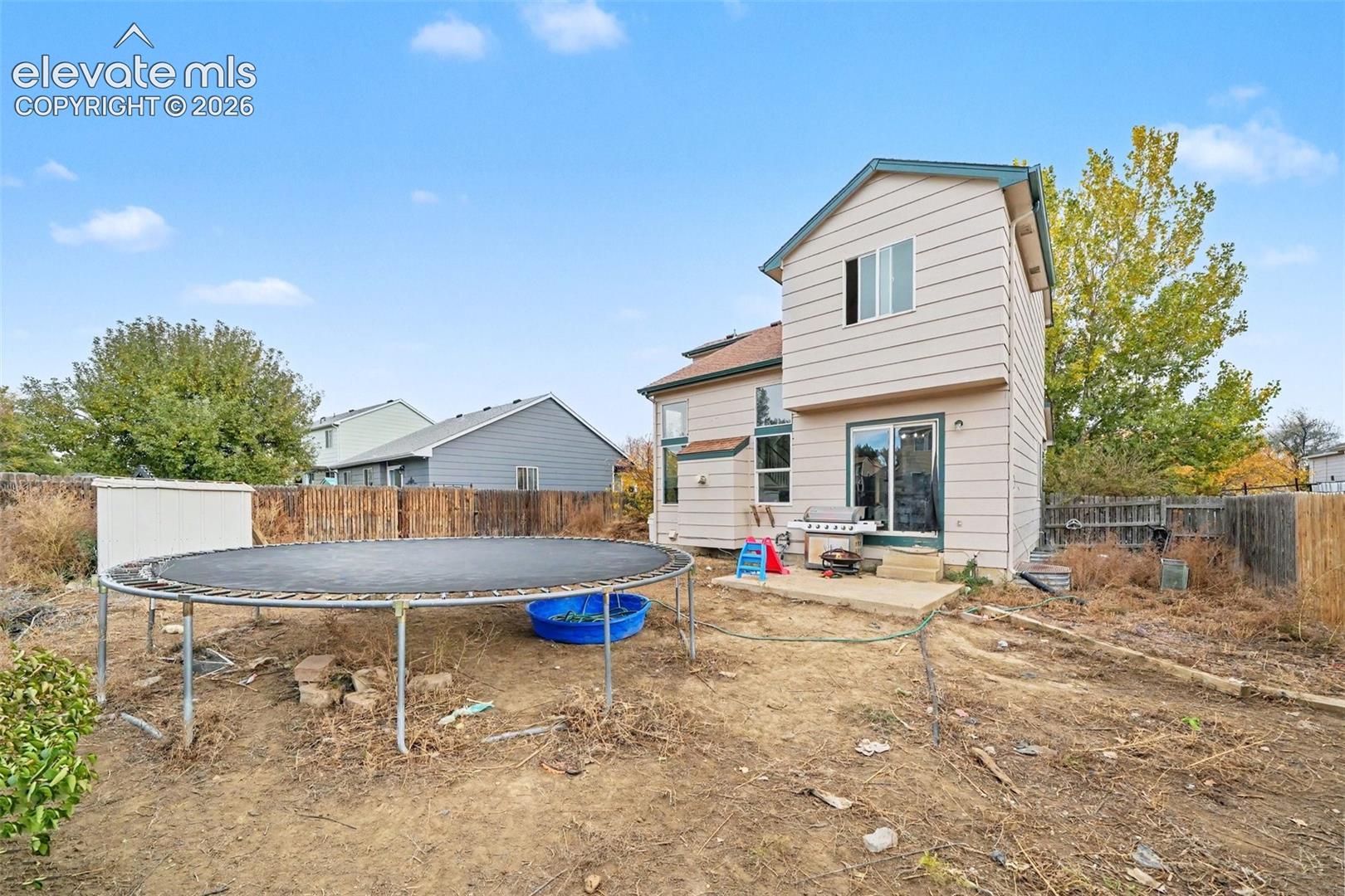 Two-story exterior featuring light-toned horizontal siding, a concrete rear patio, and wood-panel perimeter fencing