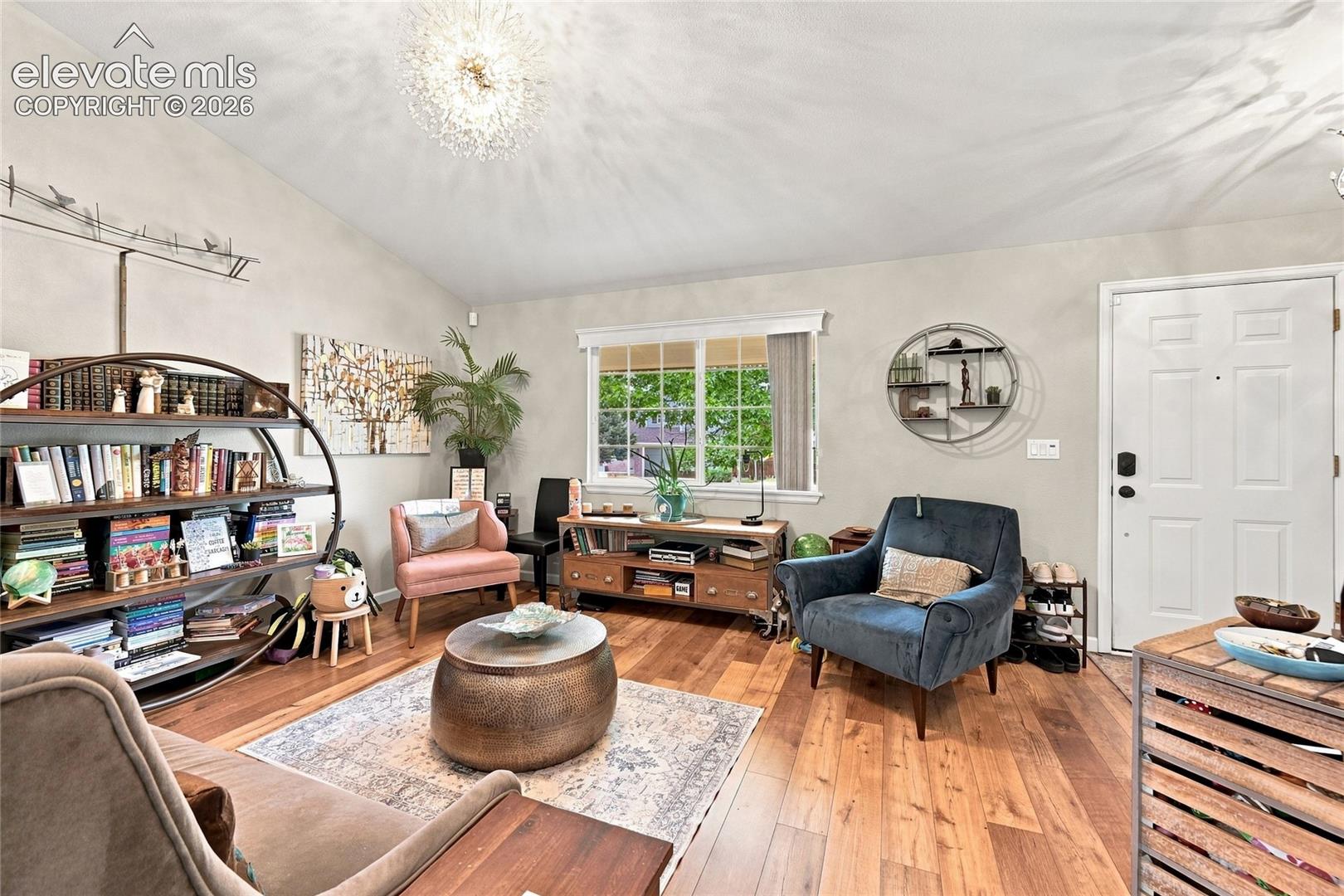 Living area featuring vaulted ceilings, wood-finish flooring, multi-pane window, and a central modern pendant light fixture